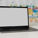 A blank laptop screen on a table with colorful sticky notes in the background.