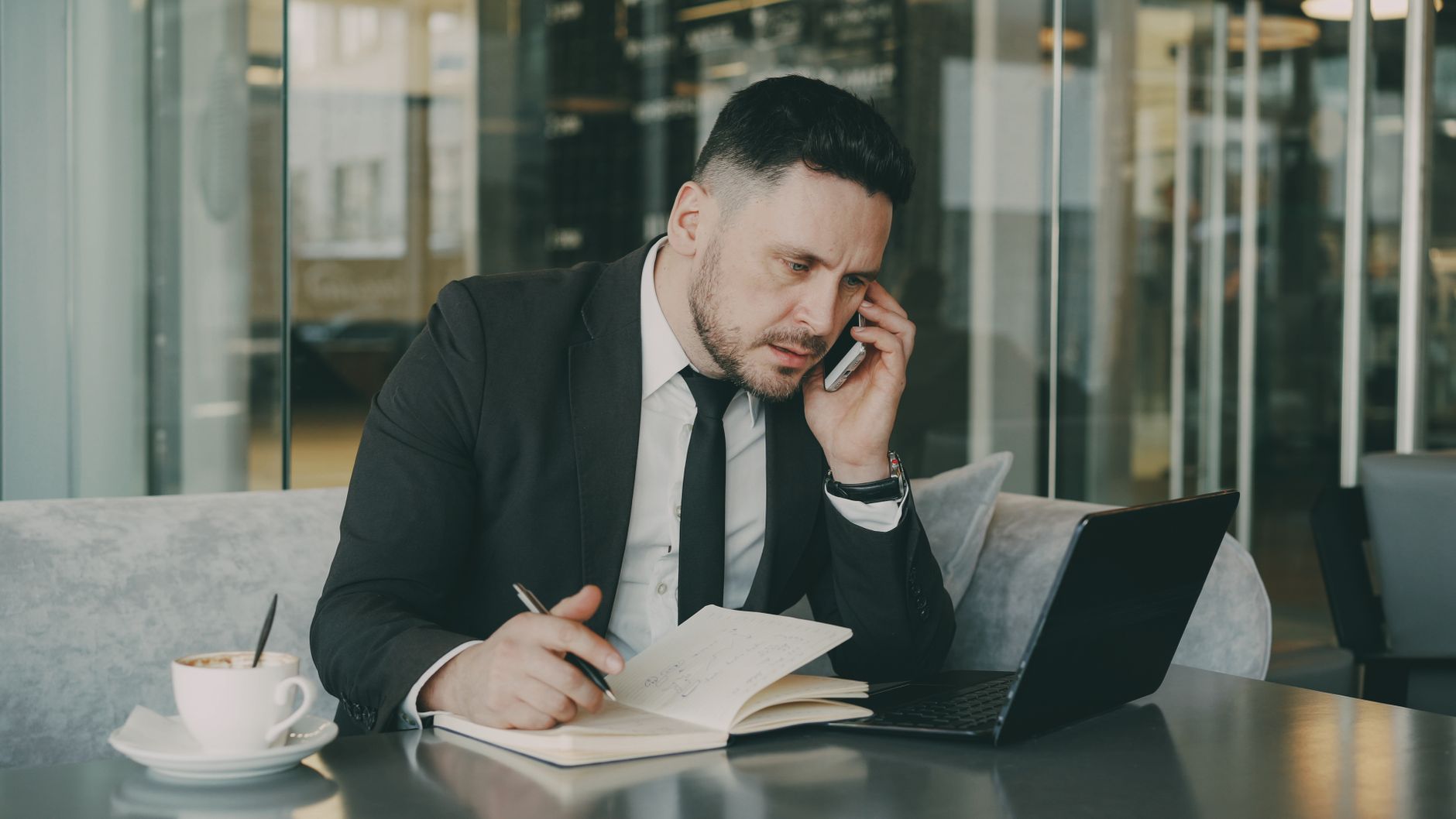 Businessman talks on phone while writing notes in a modern cafe. — Financial Flexibility: Getting a $3000 Loan with No Credit