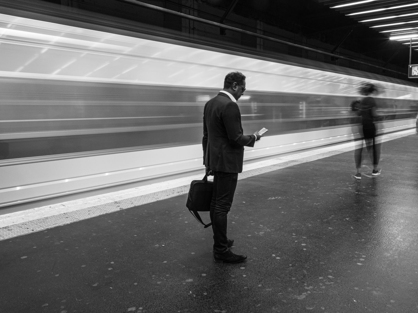 Black and white photo of a businessman at a bustling Paris metro station, holding his phone. — Protect Your Online Presence: