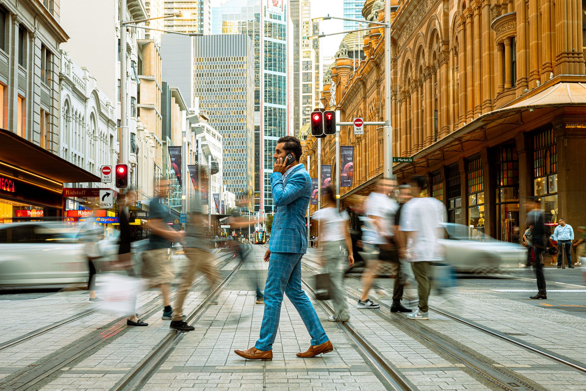A businessman in a blue suit crosses a busy street in Sydney, Australia, surrounded by motion-blurred pedestrians. — Turn Kar