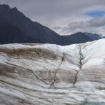 Two hikers traversing a glacier with mountains in the background